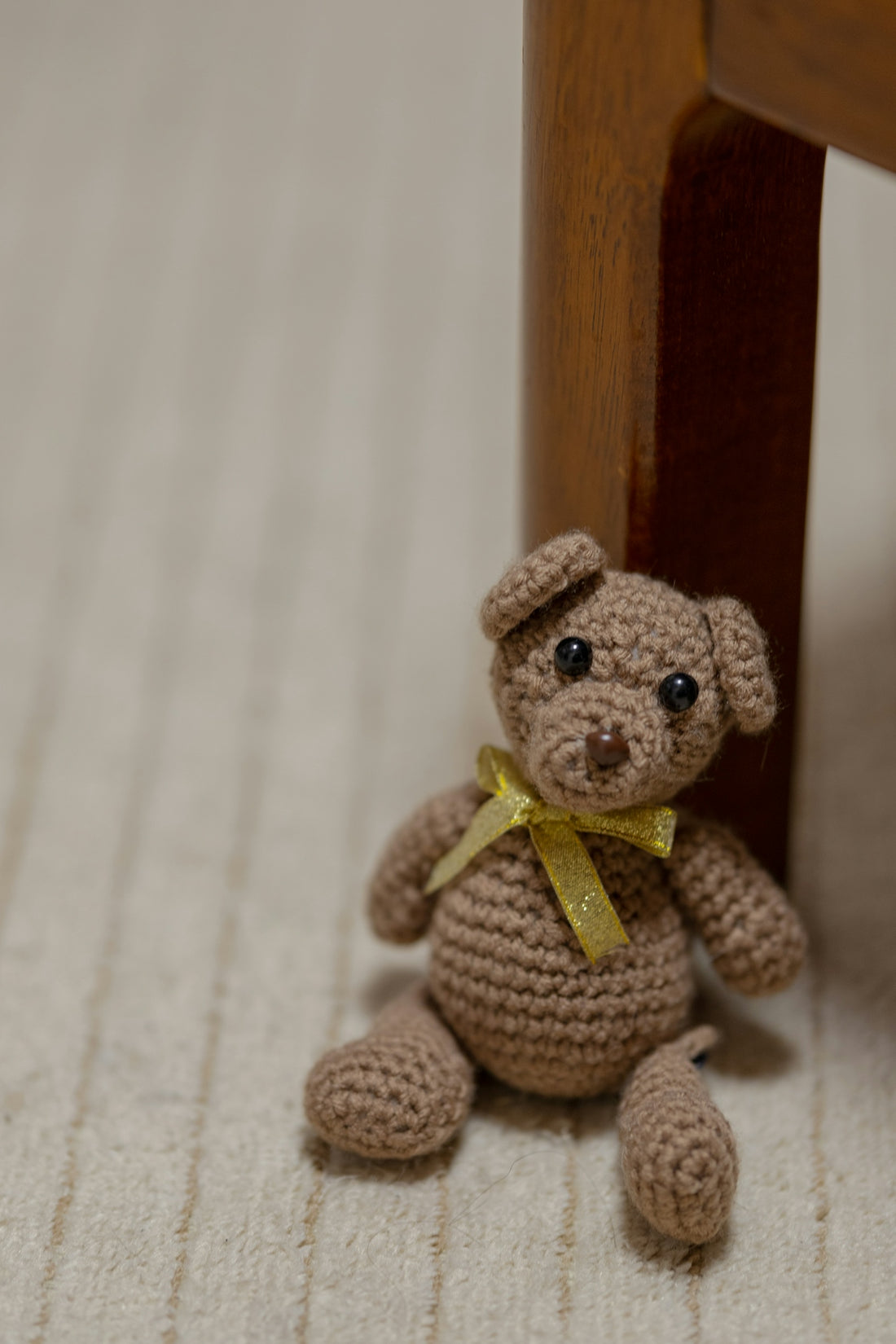 a crocheted teddy bear sitting under a wooden chair