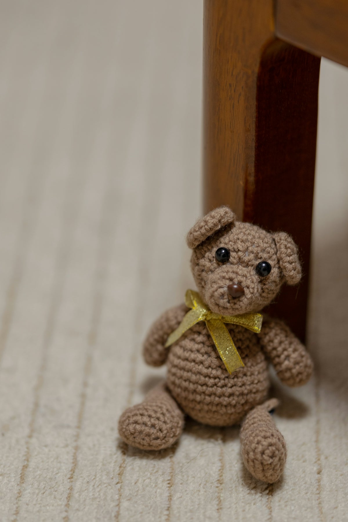 a crocheted teddy bear sitting under a wooden chair