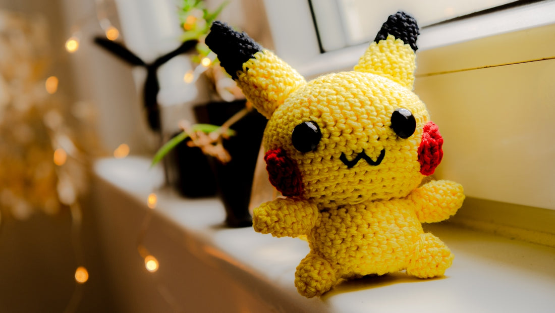 A crochet pikachu is happily displayed on a windowsill.