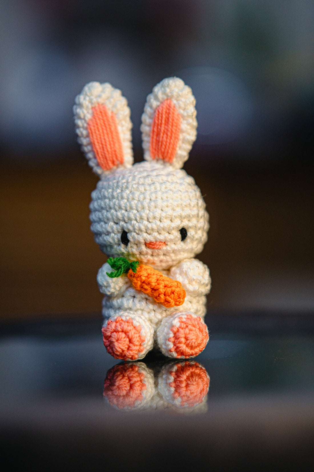 Here is a caption for the image: a crochet bunny holding a tiny carrot.