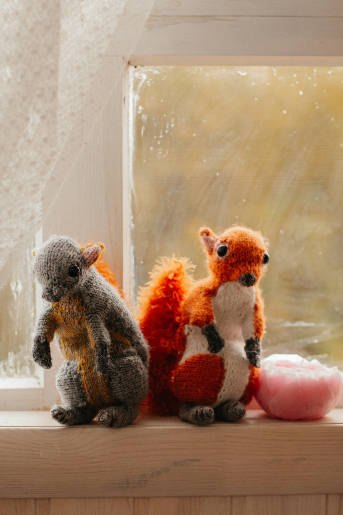 Two knitted squirrels sit on a windowsill.