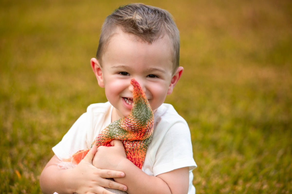 A smiling young boy holding a colorful stuffed toy.
