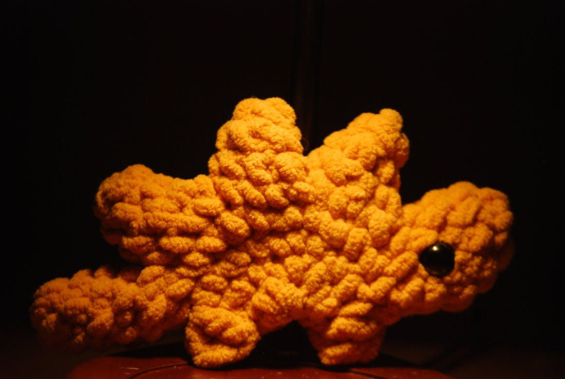 A small orange crocheted dinosaur toy with one black eye.