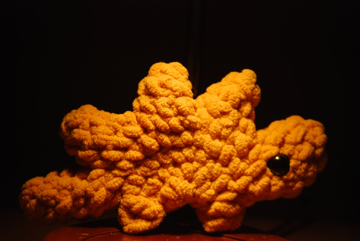 A small orange crocheted dinosaur toy with one black eye.